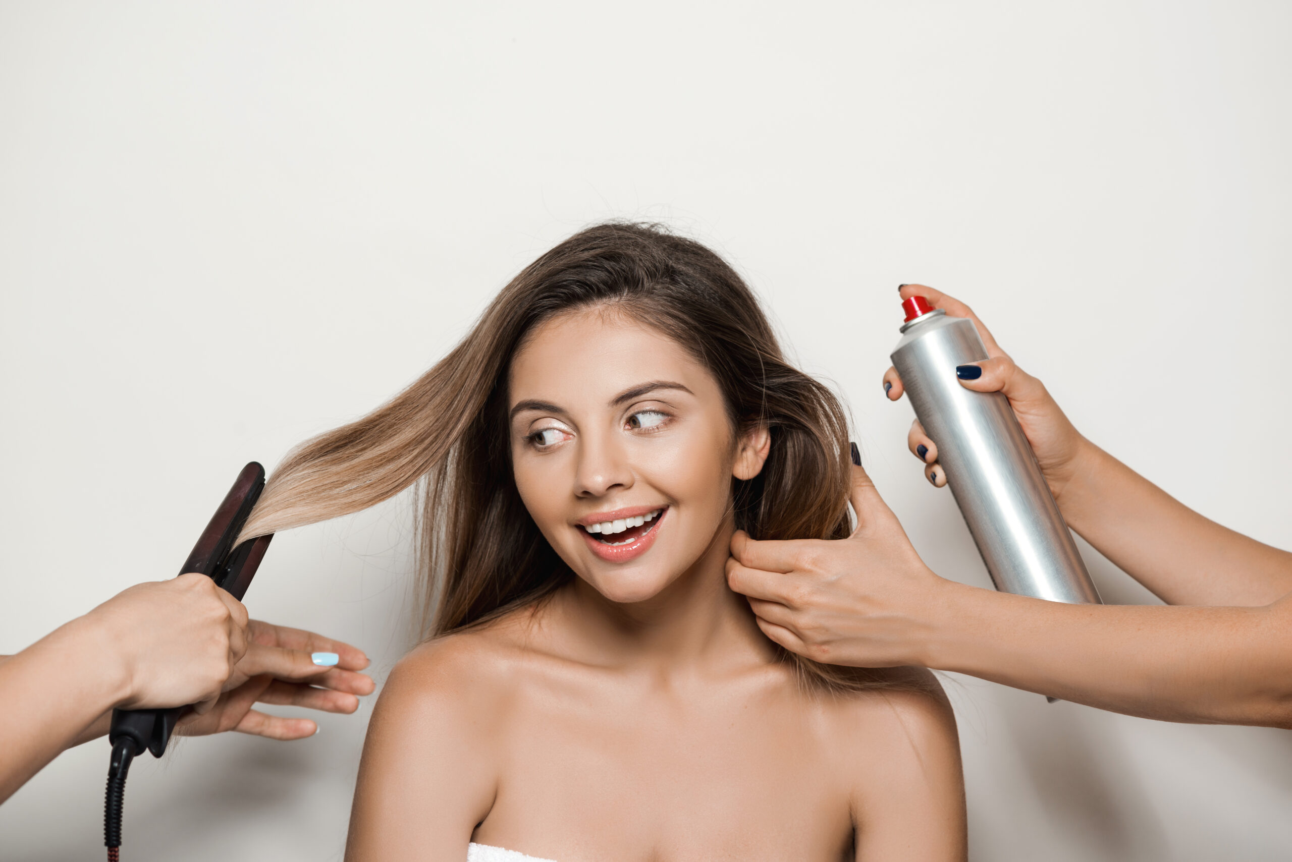 Hands doing hairstyle to young beautiful naked girl in towel over light background.